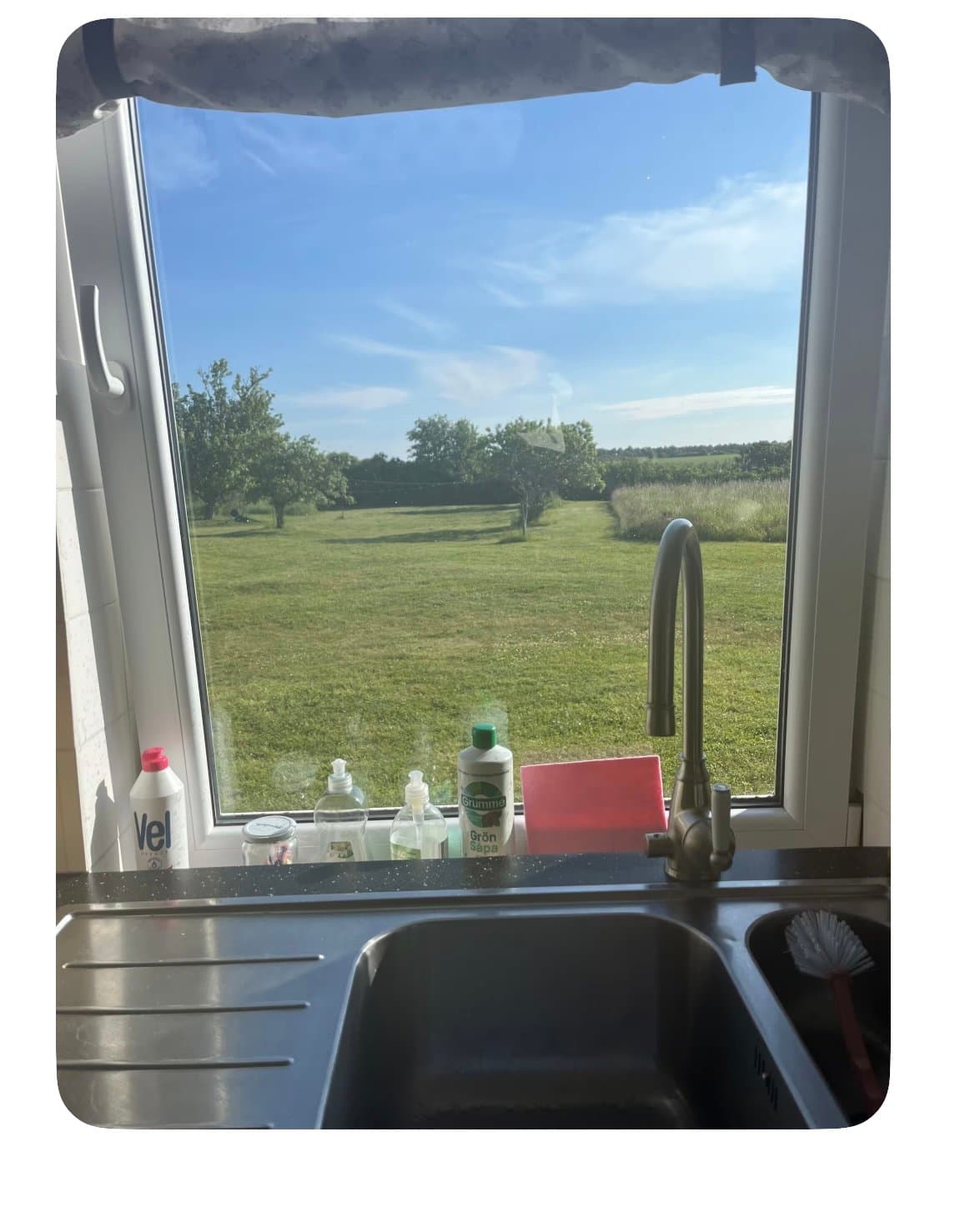 Utsikt från köket över vidsträckta gröna ängar och träd. Härlig naturomgiven miljö med öppen landskapsvy som skapar en lugn och idyllisk atmosfär.