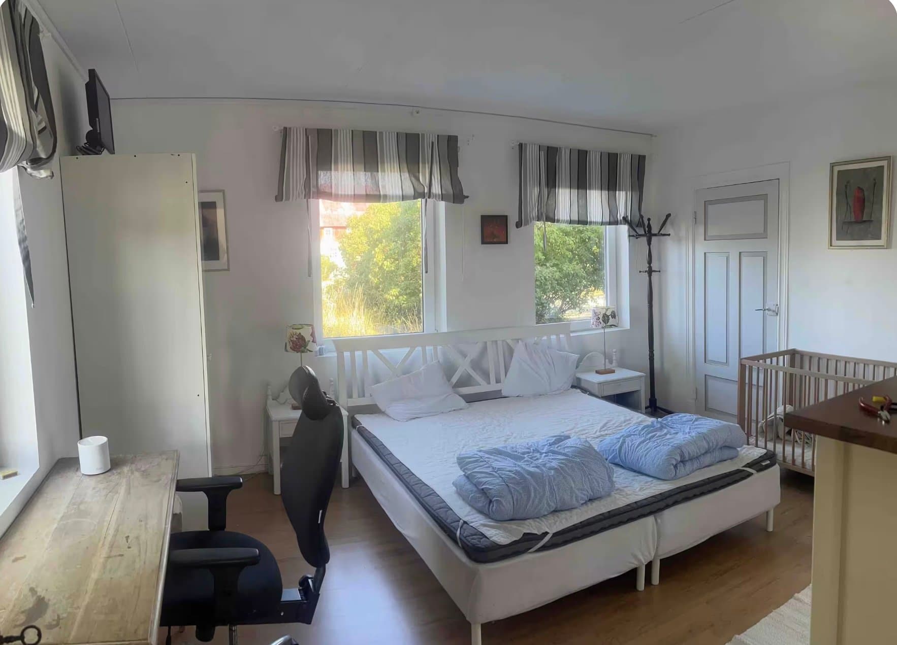 Ljust och luftigt sovrum med bekväm dubbelsäng, barnvagga och stora fönster med utsikt över den gröna trädgården. Perfekt för familjer som söker en lugn och naturlig miljö.
